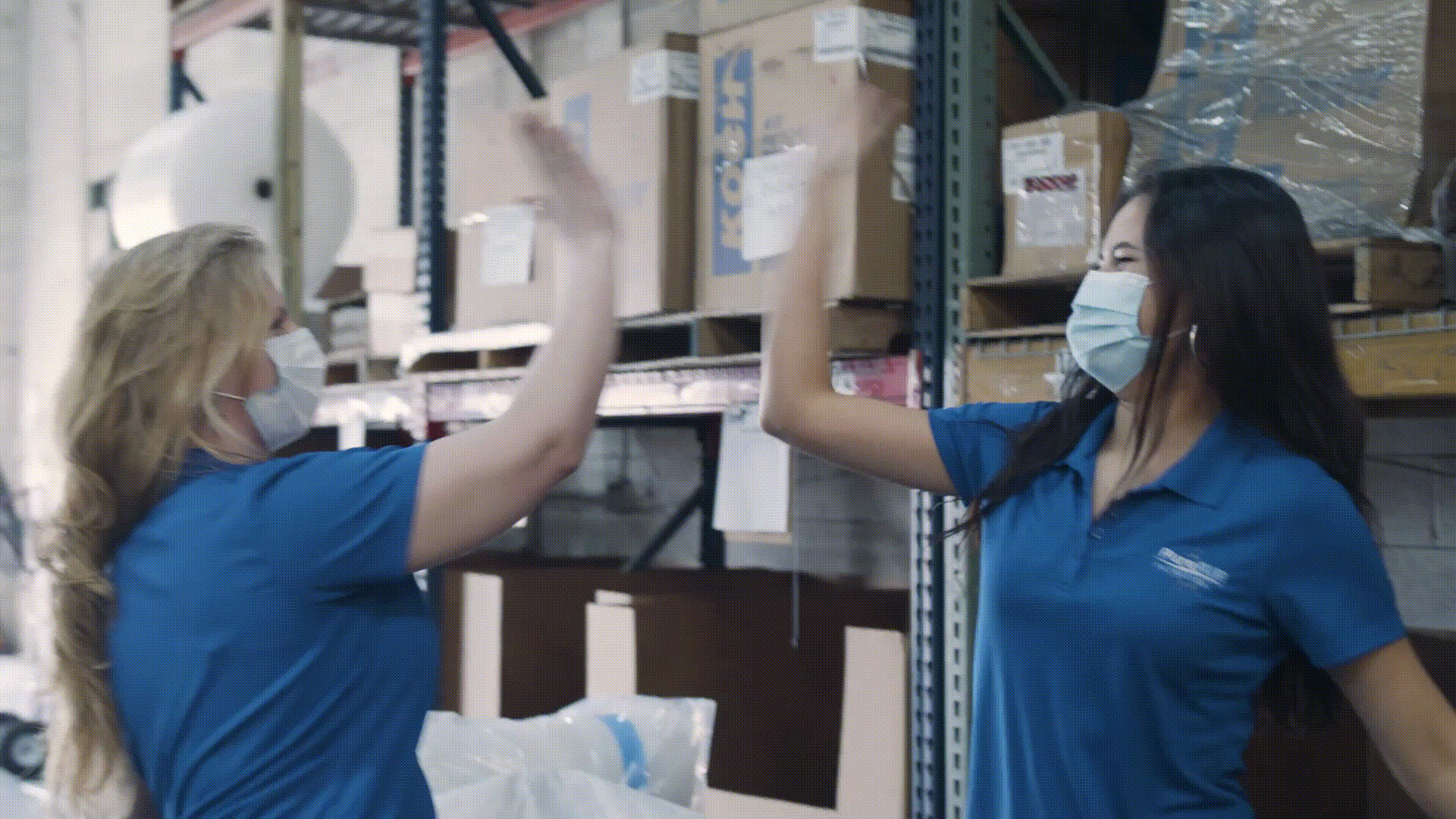 Two women in a warehouse high fiving one another